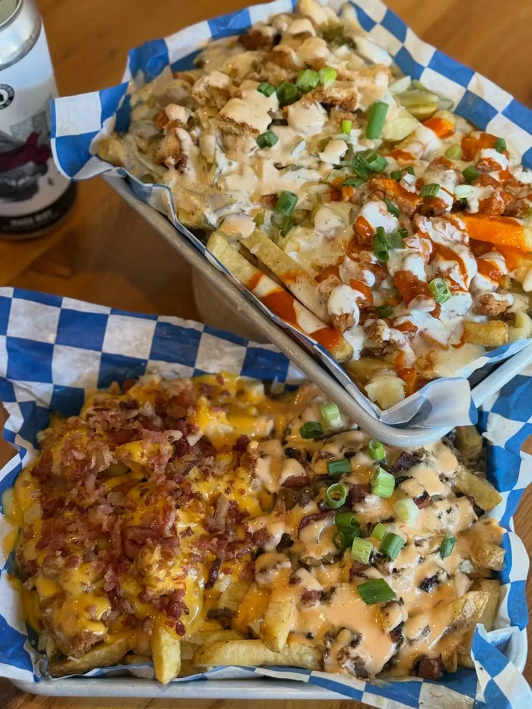 Stacked trays of loaded french fries with cheese, bacon, and diverse toppings.
