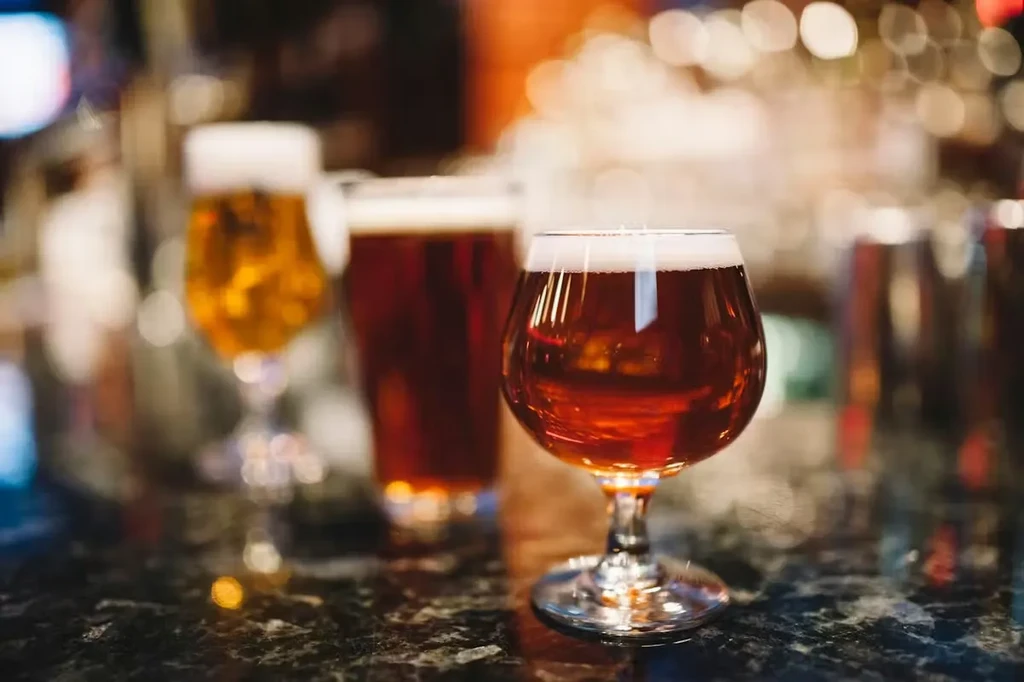 Amber beer snifter in sharp focus, two blurred beers on dark bar.