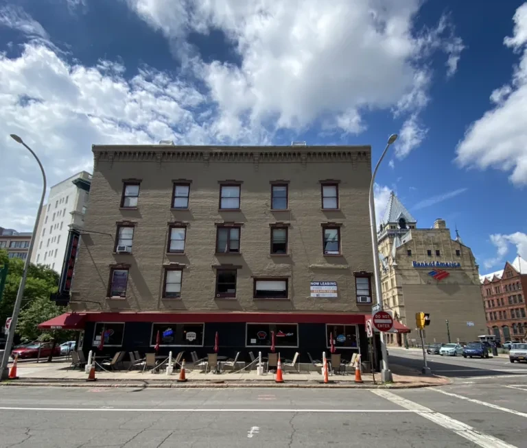 Tan brick building with red awning, outdoor seating, and Bank of America.