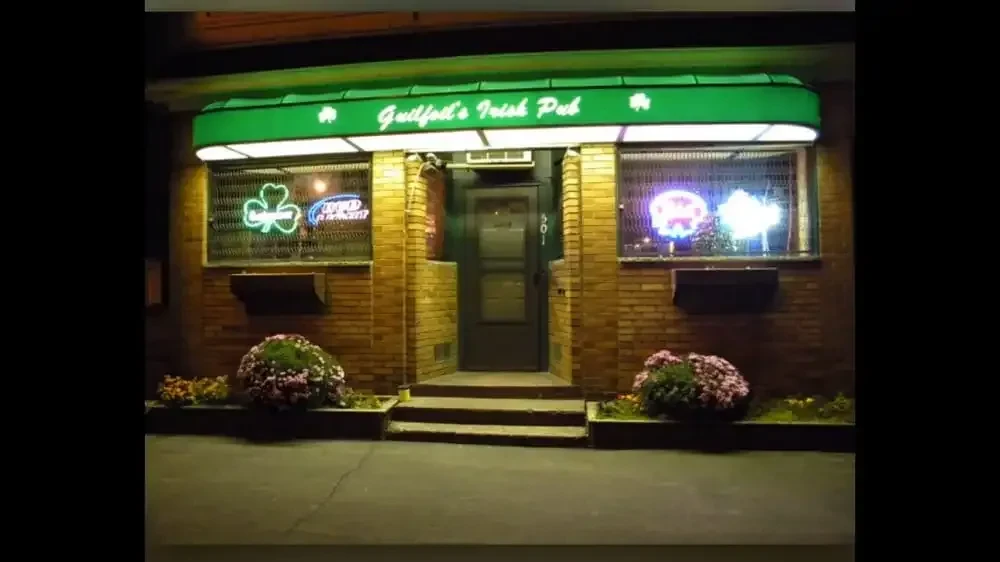 Guilford's Irish Pub storefront at night with neon signs and flowers.