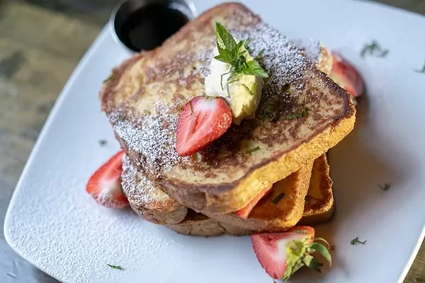 Stack of French toast with strawberries, powdered sugar, and mint.