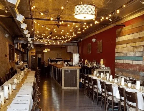 Restaurant interior with set tables, patchwork wall, red wall, string lights.