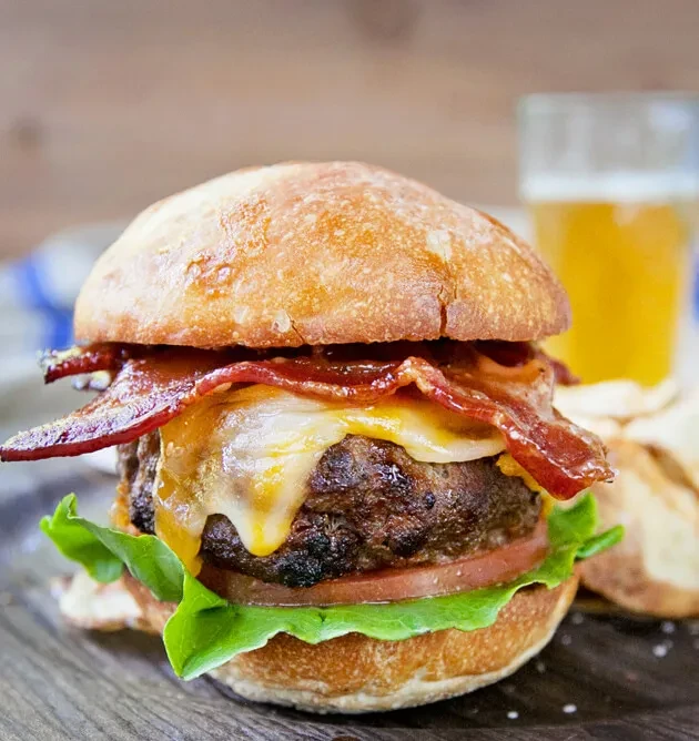A thick bacon cheeseburger with melted cheese, crispy bacon, beer, and chips.