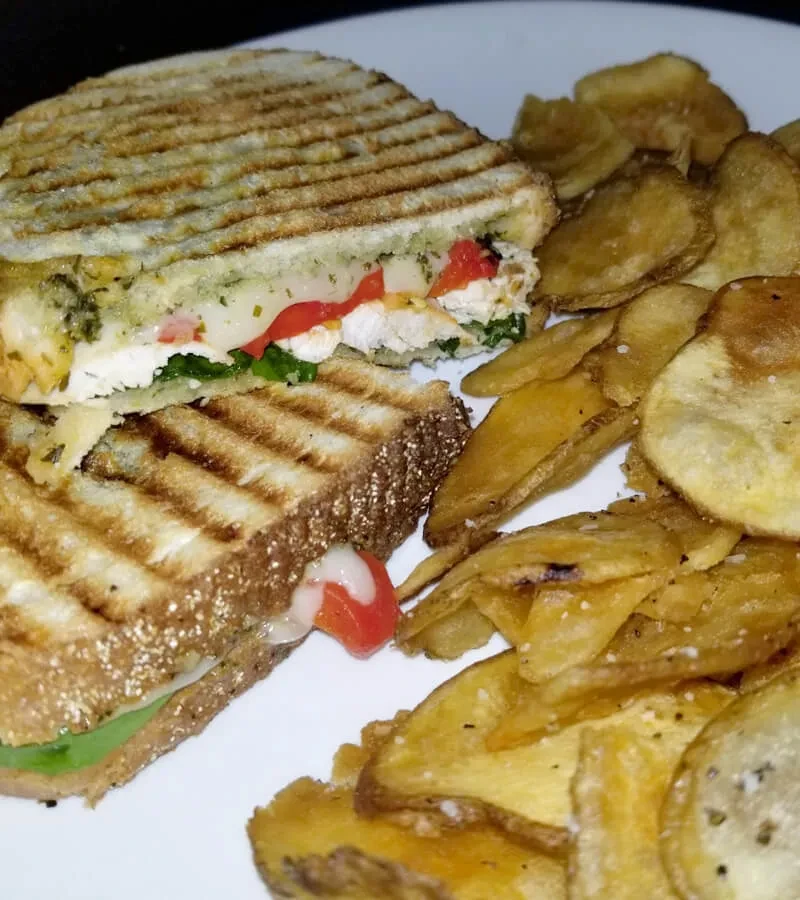 Half-cut grilled sandwich with chicken, cheese, vegetables, and potato chips.