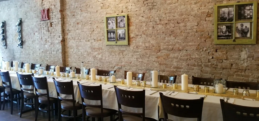 Candlelit dining table with chairs against an exposed brick wall.