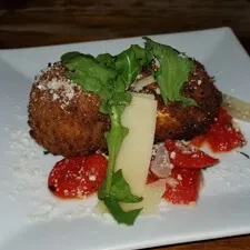 Two deep-fried fritters with cheese, arugula, and diced red peppers.