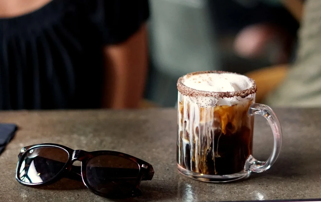 Close-up of an iced drink with white foam, garnished rim, sunglasses.