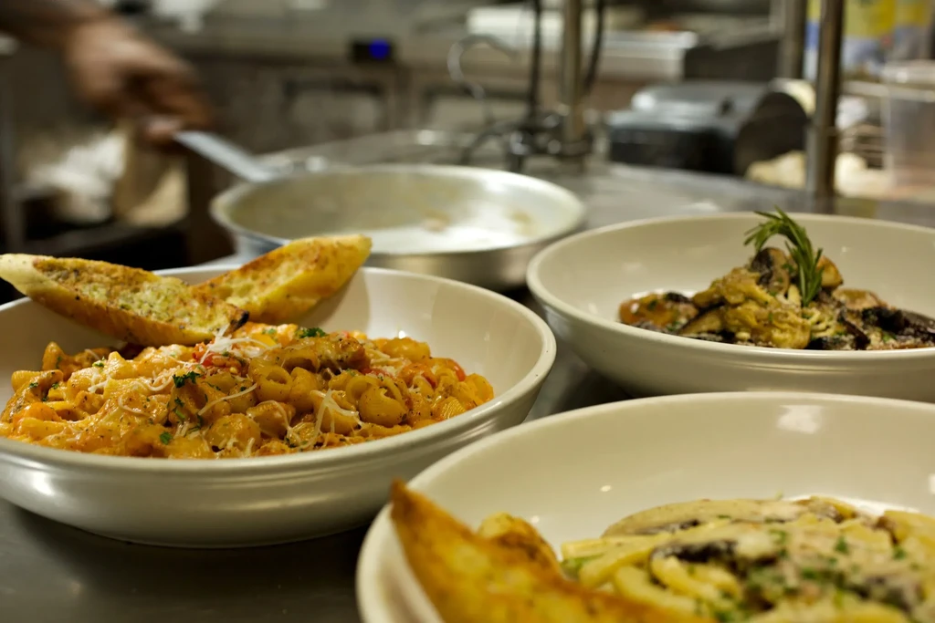 Three pasta bowls, including mac and mushroom, on steel counter.