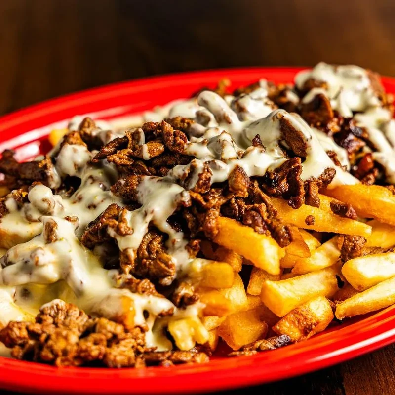 French fries topped with seasoned meat and cheese sauce on a red plate.