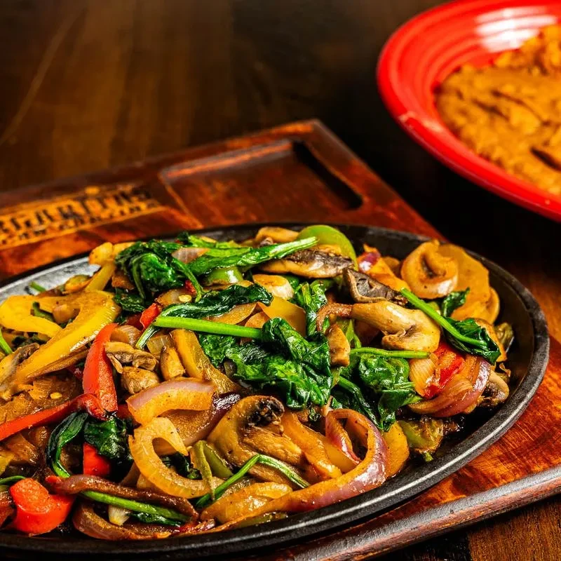 Sizzling fajita-style vegetables in a cast iron pan on a wooden board.