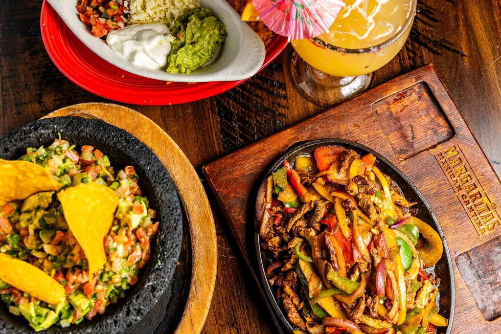 Overhead view of a Mexican meal: fajitas, guacamole, sides, margarita.
