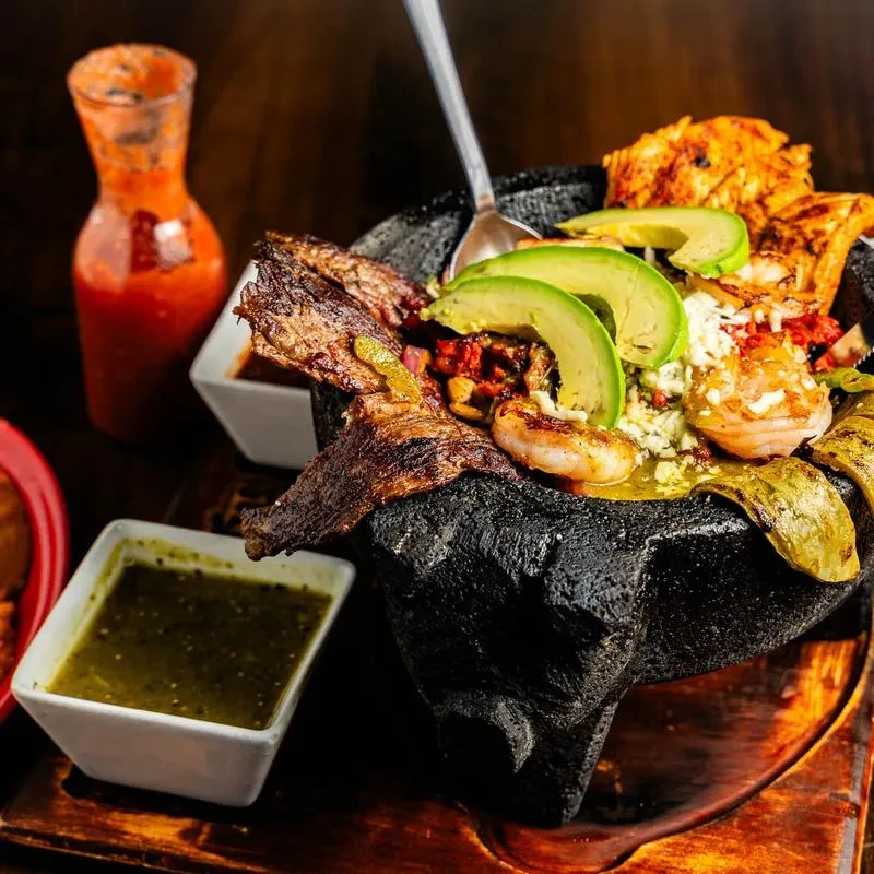 Molcajete filled with grilled steak, shrimp, chicken, avocado, cheese, and salsas.