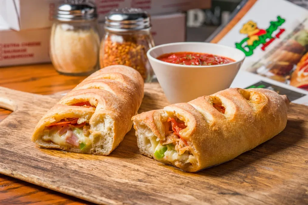Two baked stromboli halves, filled with cheese, ham, peppers, with marinara.