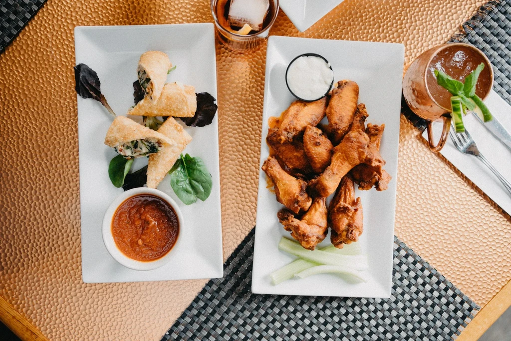 Plates of fried spring rolls and chicken wings with drinks.