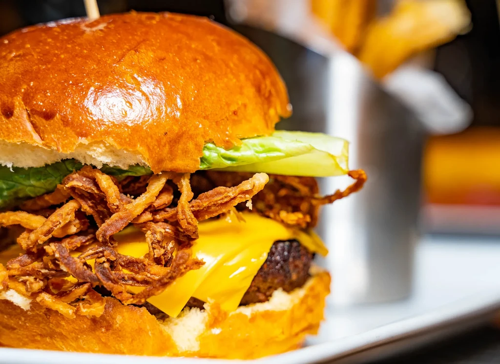 A close-up of a cheeseburger with fried onions, lettuce, and a brioche bun.