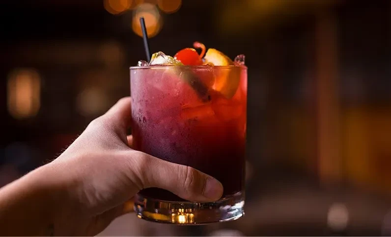 Frosted red cocktail with ice and cherry, held by a hand.