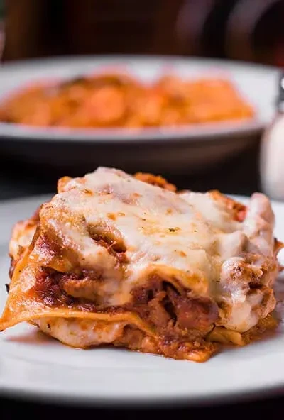 Generous lasagna slice with red sauce, melted cheese, and green herbs.