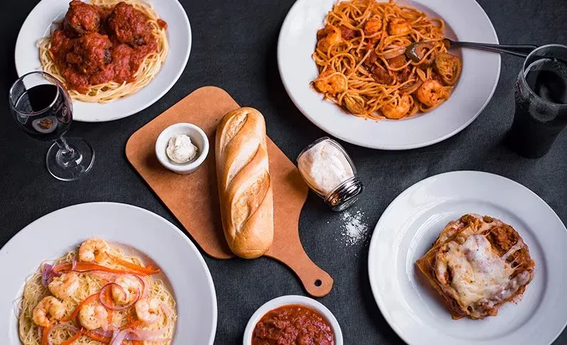 Various Italian pasta dishes, bread, and drinks on a dark table.