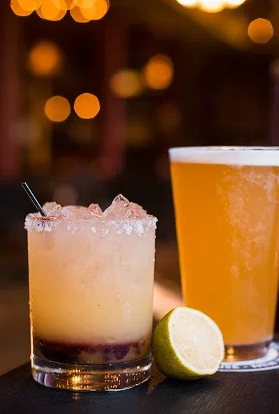 Layered cocktail, pint of amber beer, and lime half on bar.