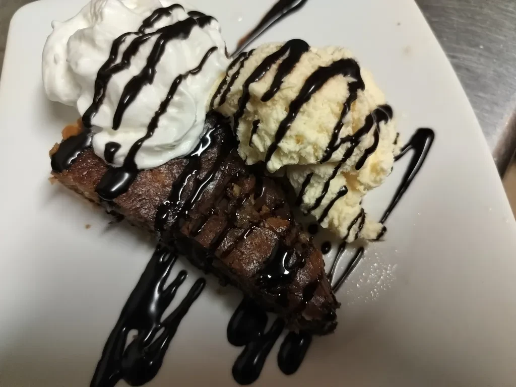 Chocolate dessert wedge with whipped cream, vanilla ice cream, chocolate drizzle.