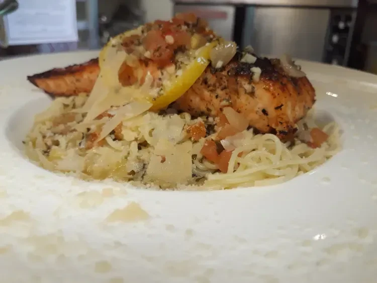 Spaghetti with grilled salmon fillet, topped with salsa, lemon, and Parmesan.