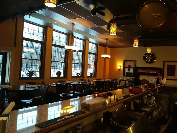Warmly lit restaurant interior with bar, dining tables, and snowy winter windows.