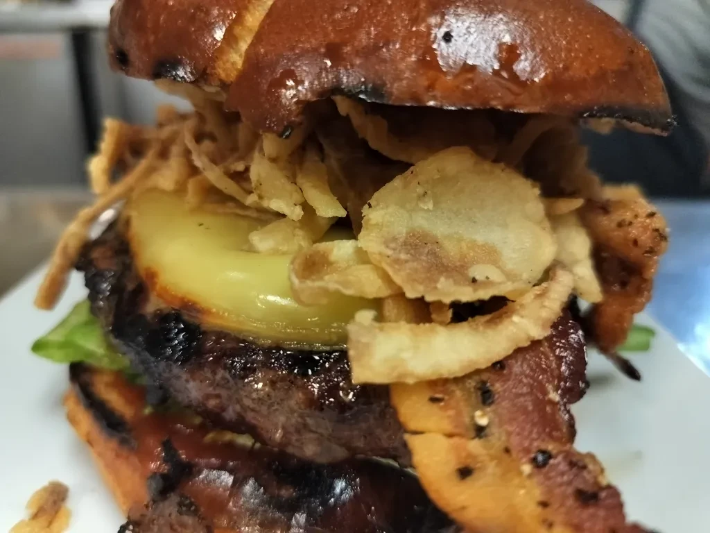 Elaborately stacked gourmet burger with pineapple, bacon, and onion strings.