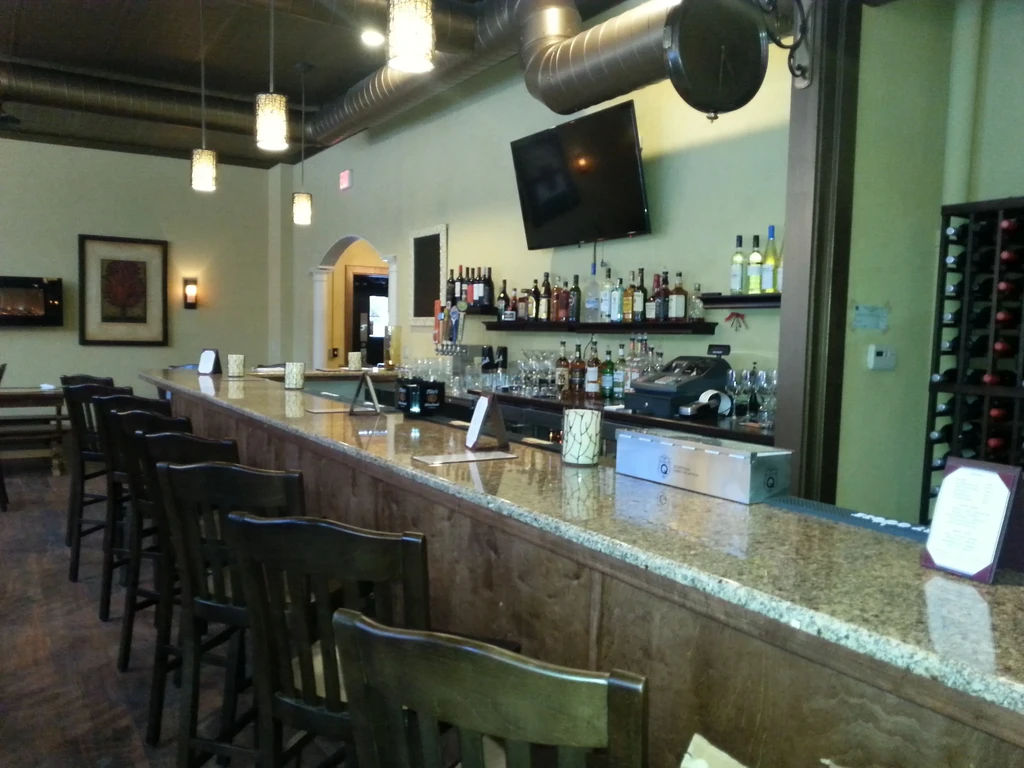 Empty bar interior with long granite counter, dark stools, and liquor display.