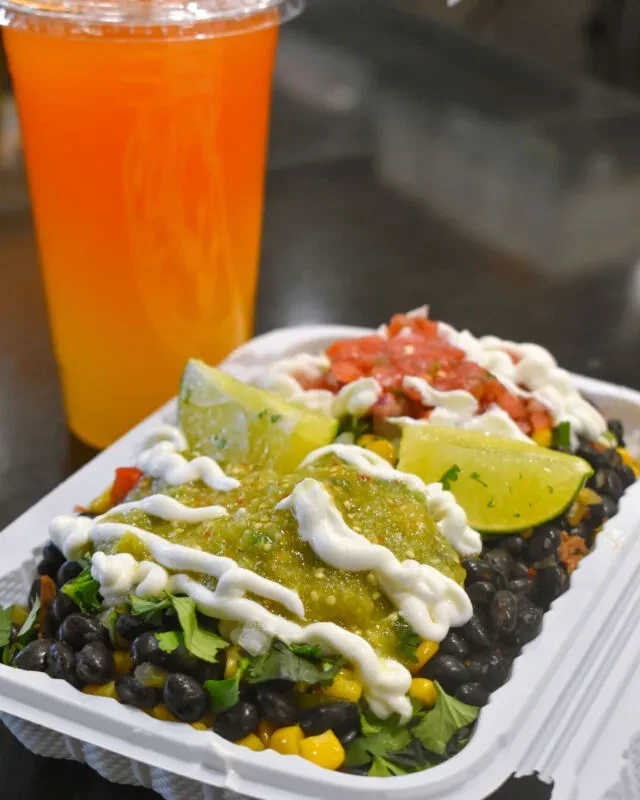 Two colorful burrito bowls with lime, salsa, and orange drink.