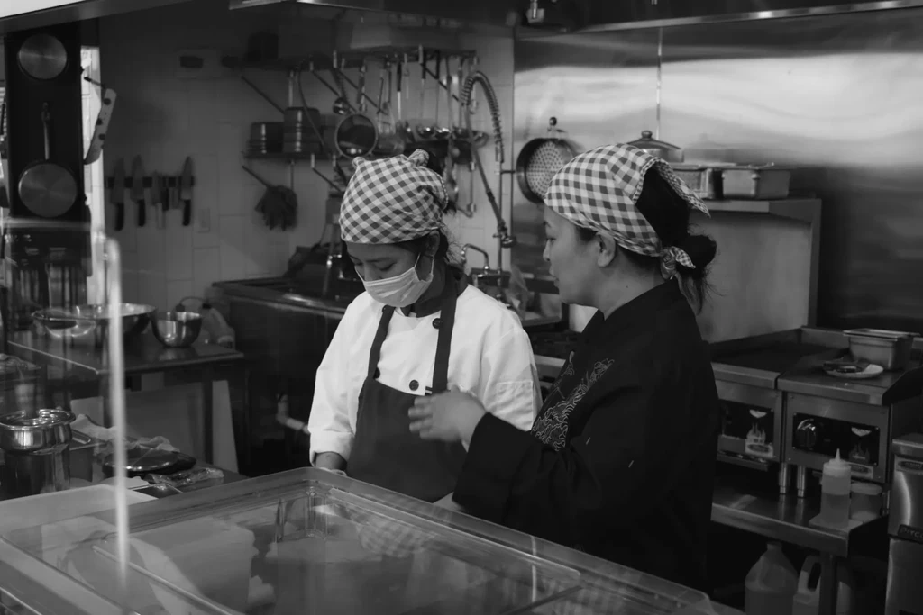 Two women chefs in black and white kitchen conversation.