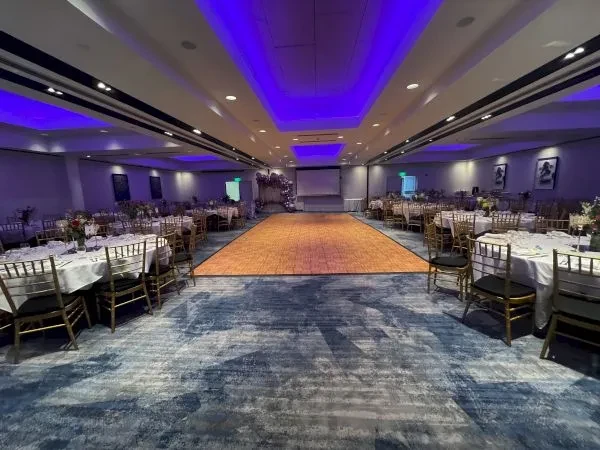 A large ballroom with dining tables, a dance floor, and purple lighting.