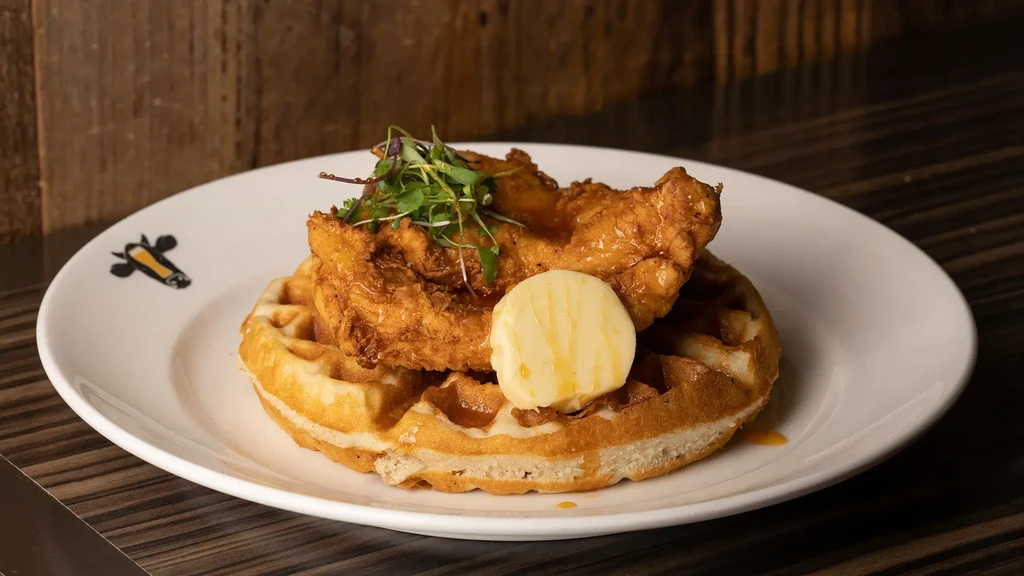 Chicken and waffle dish with butter, syrup, and microgreens.