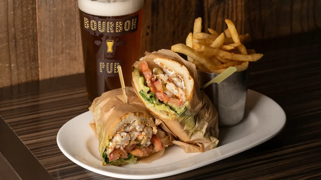 A sandwich, fries, and beer on a white plate and dark table.