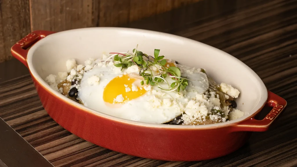 Red baking dish with two fried eggs, crumbled cheese, and microgreens.