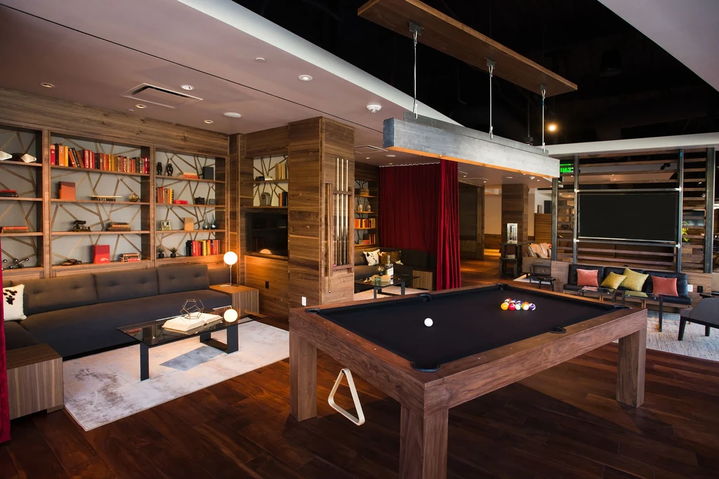 A modern lounge with a pool table, dark wood, and red curtains.