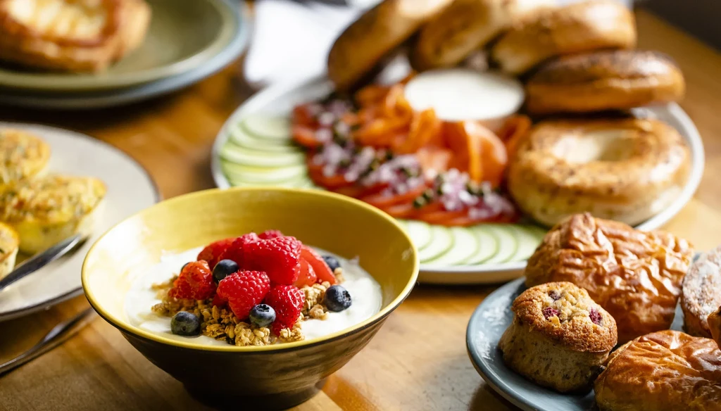 Assorted breakfast foods including yogurt with fruit, bagels, and pastries.