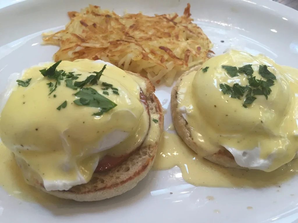 Two eggs benedict with hash browns on a white plate.