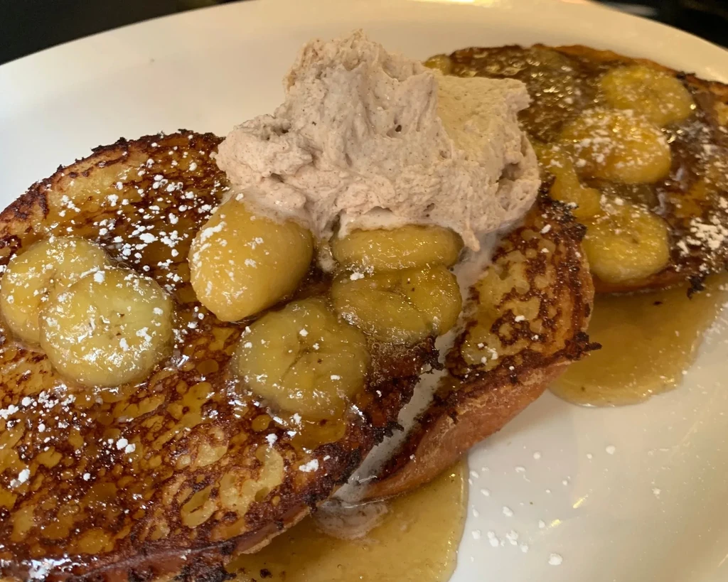 French toast with bananas, syrup, powdered sugar, and whipped cream.