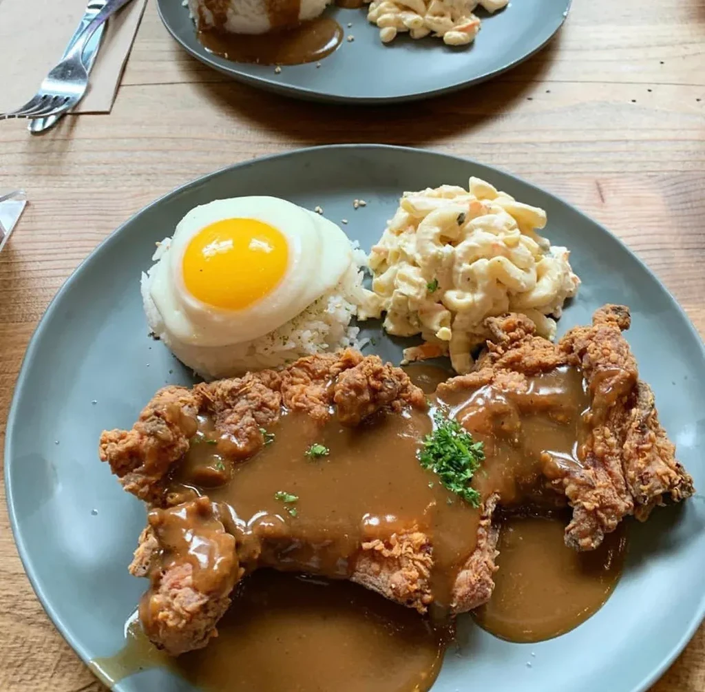 A plate with fried chicken, gravy, fried egg, rice, and macaroni salad.