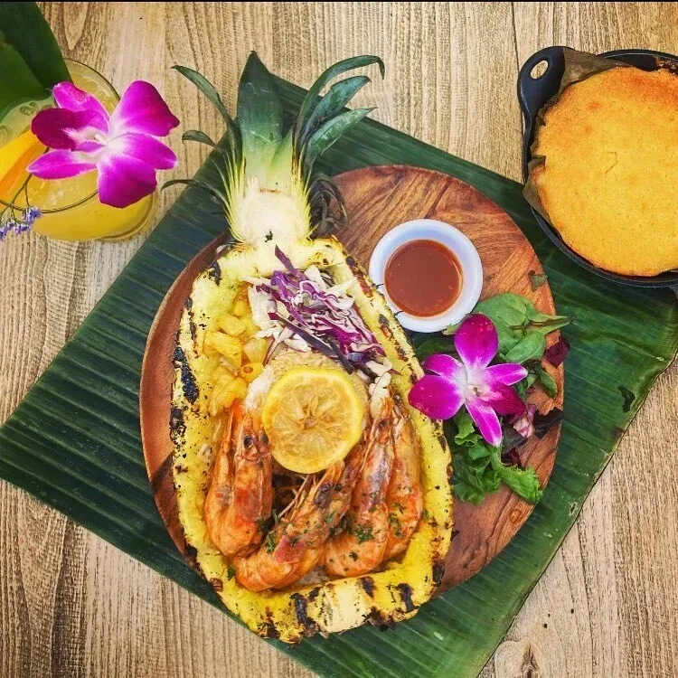 Grilled shrimp and rice served in a pineapple half with a side.