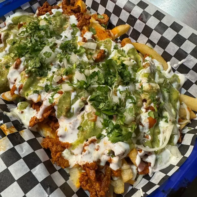 Fries topped with meat, white sauce, green sauce, cilantro, and onions.