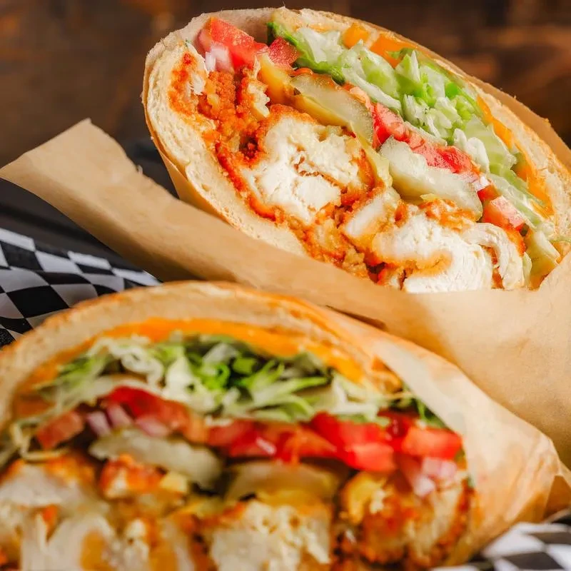 Two chicken sandwiches with lettuce, tomatoes, and sauce in parchment paper.