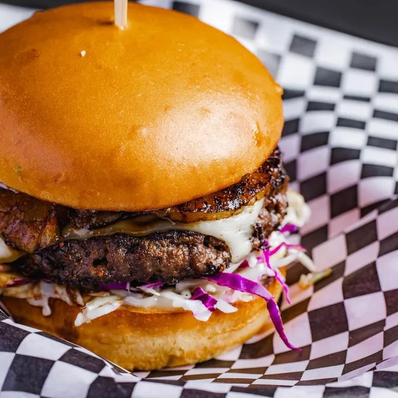 A cheeseburger with cabbage and grilled pineapple in checkered paper.