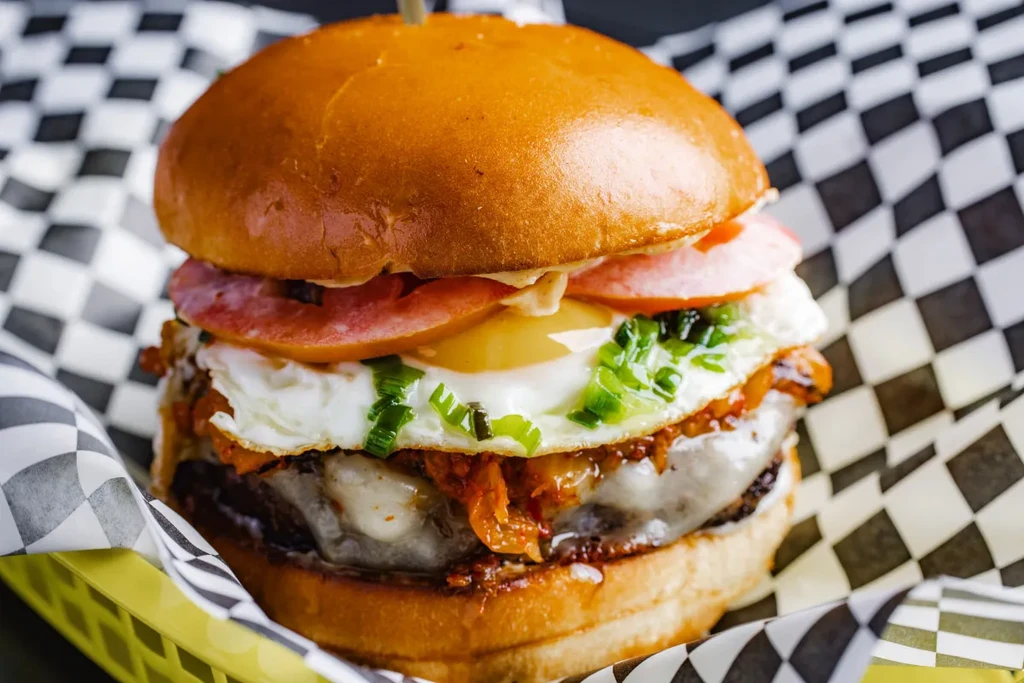 A burger with cheese, kimchi, a fried egg, and tomatoes.