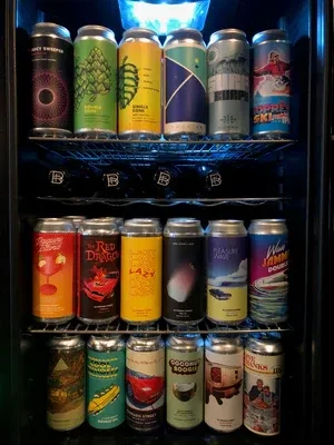 A brightly lit refrigerator full of various craft beer cans.