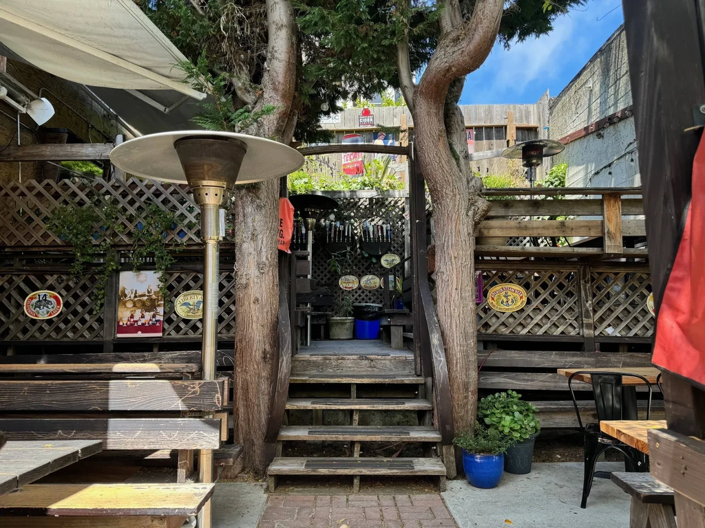 A cozy, rustic outdoor patio with wooden benches, stairs, and two trees.