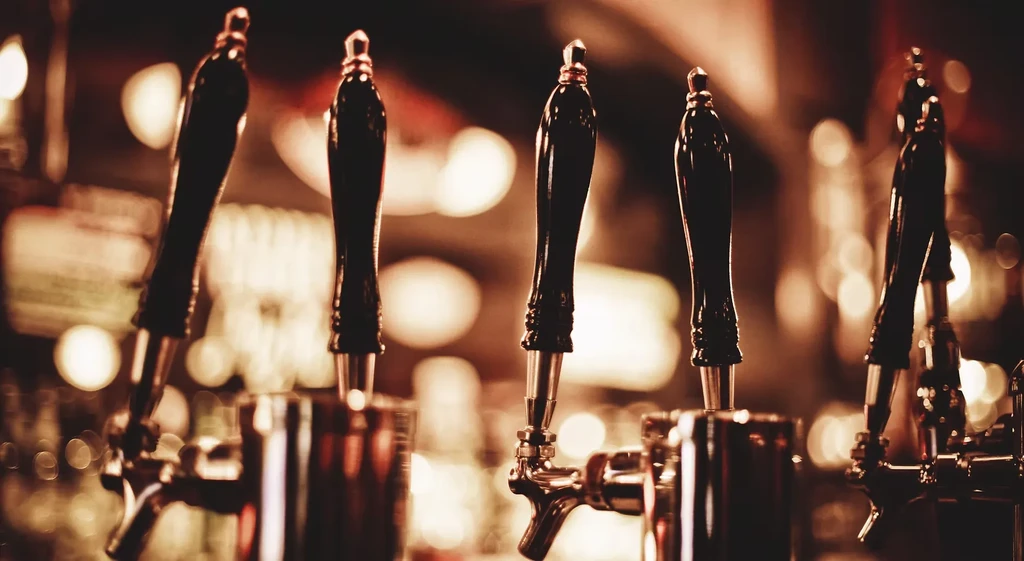 Five beer tap handles on a dark bar with bokeh lights.