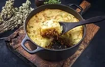 A black pot of shepherd's pie, with a serving spoon taking a portion.