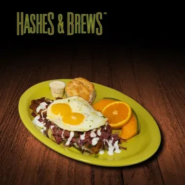 Breakfast plate with corned beef hash, fried eggs, biscuit, and fruit.