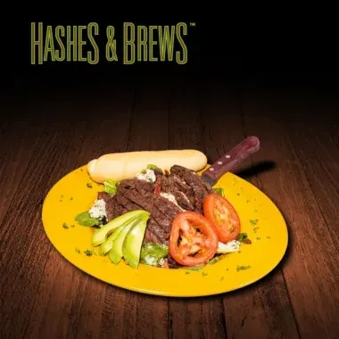 Steak salad with avocado, tomatoes, bread, and knife on yellow plate.